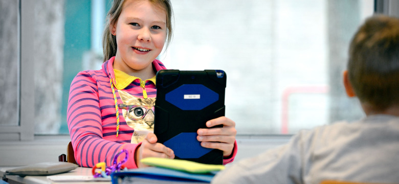 Leerling achter haar bureau met een iPad in haar handen
