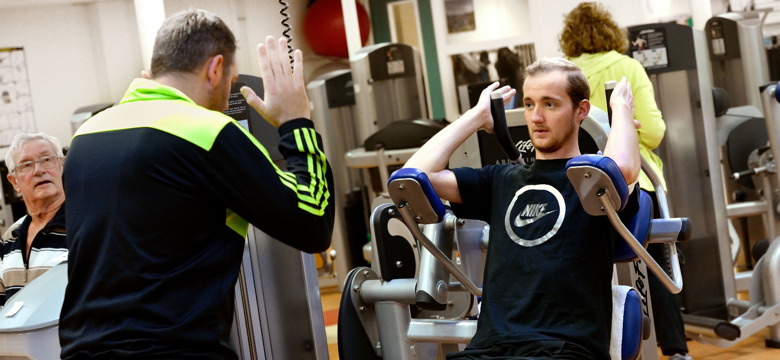 Cliënt wordt begeleid door therapeut op een fitnesstoestel