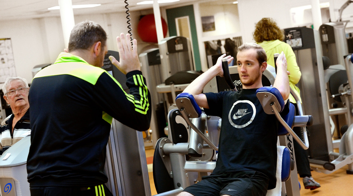 Cliënt wordt begeleid door therapeut op een fitnesstoestel